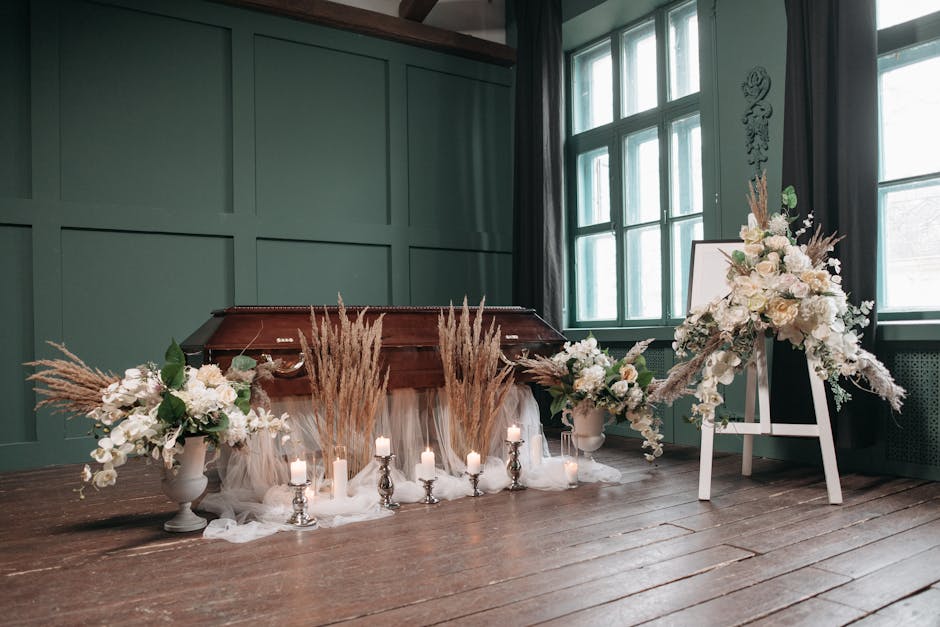 A floral arrangement featuring white roses, lilies, and orchids complemented by soft beige pampas grass and greenery, displayed in white vases and placed symmetrically on either side of a wooden coffi