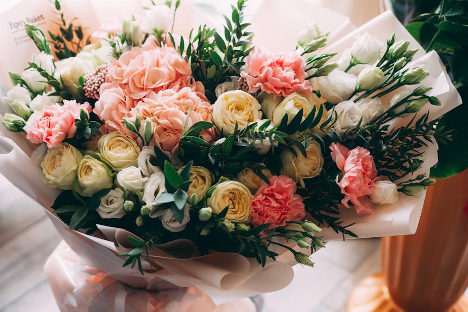 A floral arrangement featuring a bouquet of fresh flowers including pale pink hydrangeas, cream and white roses, and light pink carnations, accented with greenery such as fern leaves and eucalyptus sp
